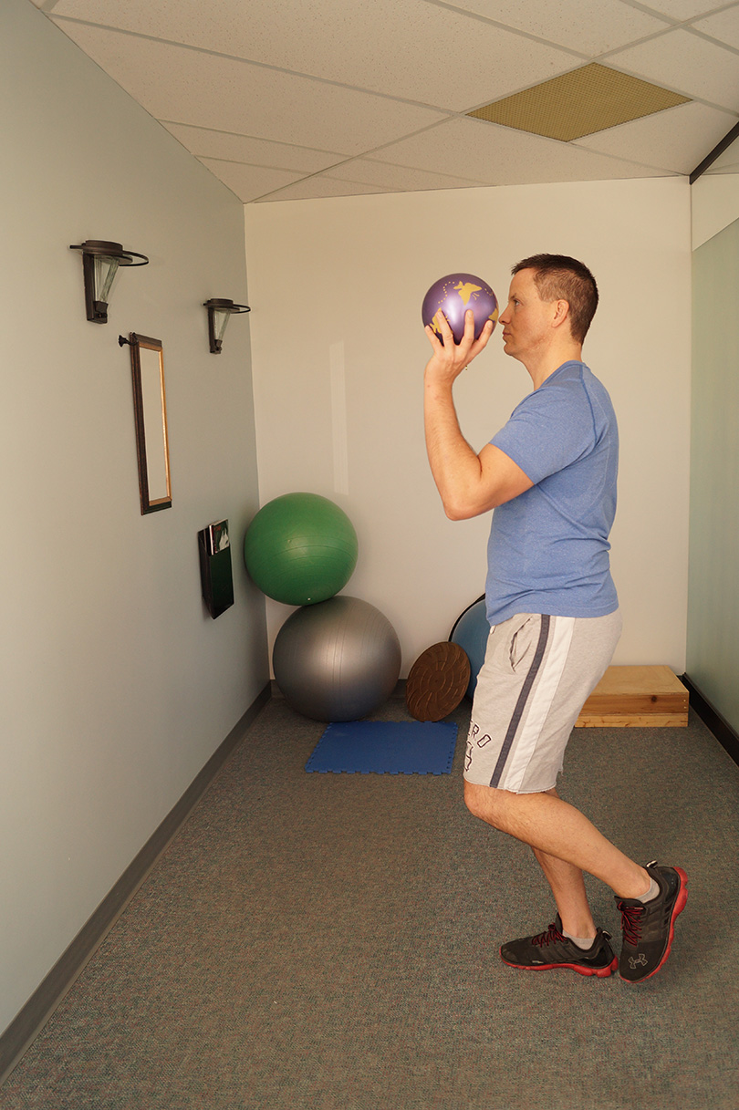 Man balancing on one foot with it lifted slightly in the air preparing to throw a ball against the wall with the same arm as the leg that is lifted.