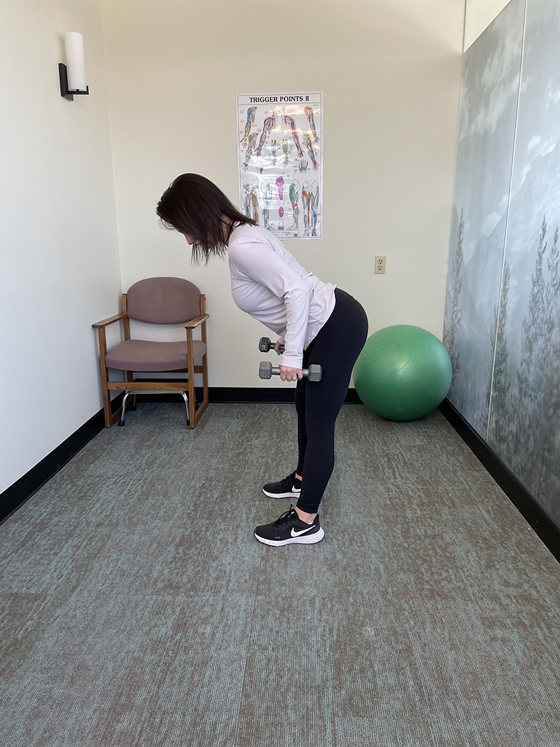 Woman bending over with a straight back and stretching while holding weights at her side.