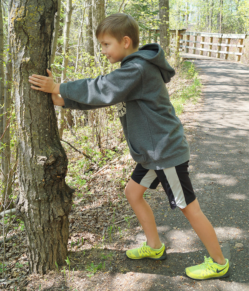 Person stretching their calf outside using a tree for support.