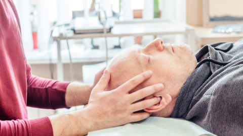 Therapist treating patient using craniosacral therapy treatment techniques. The therapist has their hand placed on mans head.